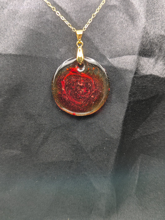 Red colored circle resin pendant with a coral colored pigment swirled in it, with a gold pinch bail on a gold plated metal chain.