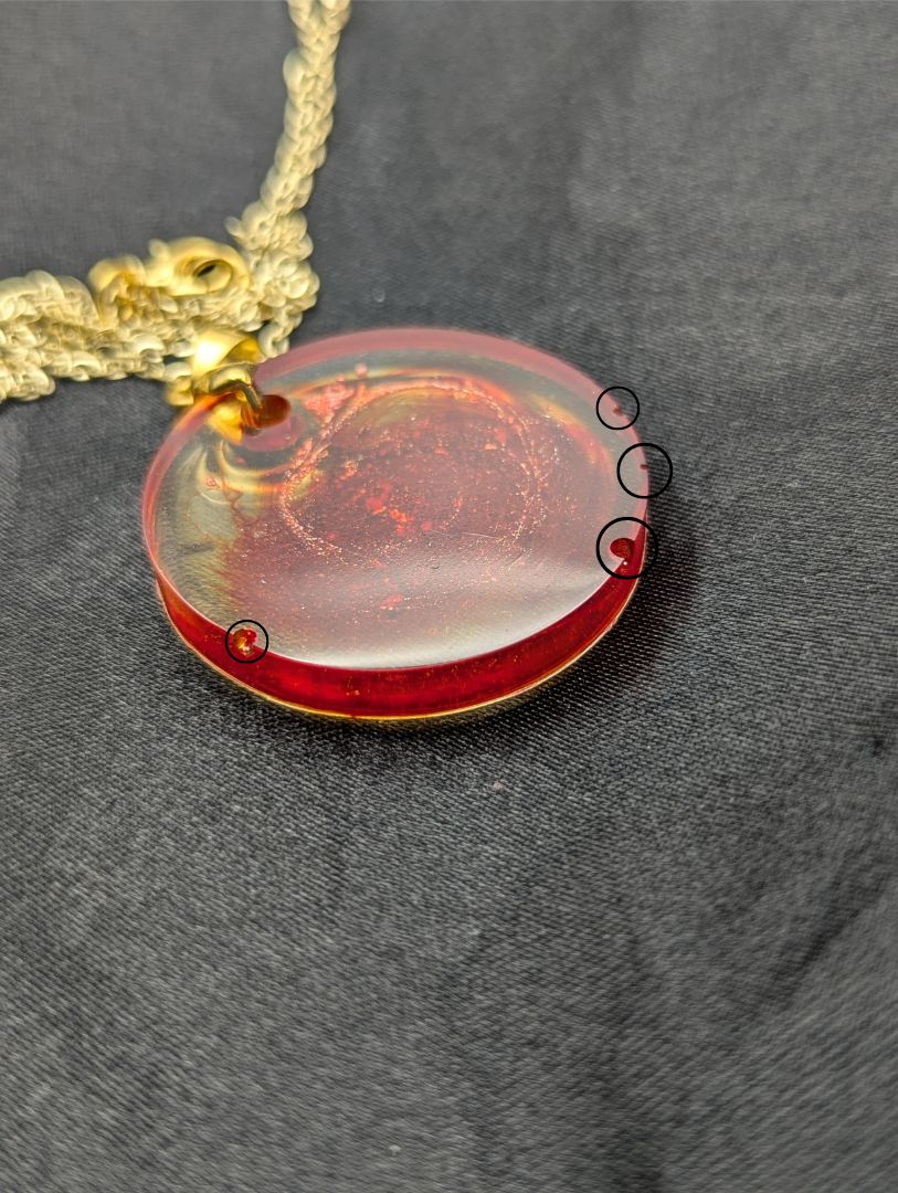 Red colored circle resin pendant with a coral colored pigment swirled in it, with a gold pinch bail on a gold plated metal chain.
