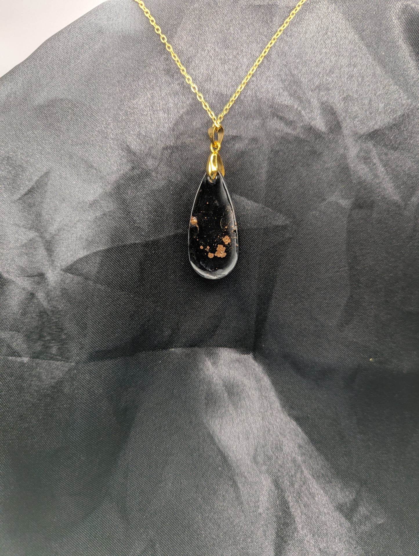 Back view of Black Resin Teardrop Pendant with specks of sparkly gold swirled inside. Pendant is on a gold pinch bail & gold plated metal chain.