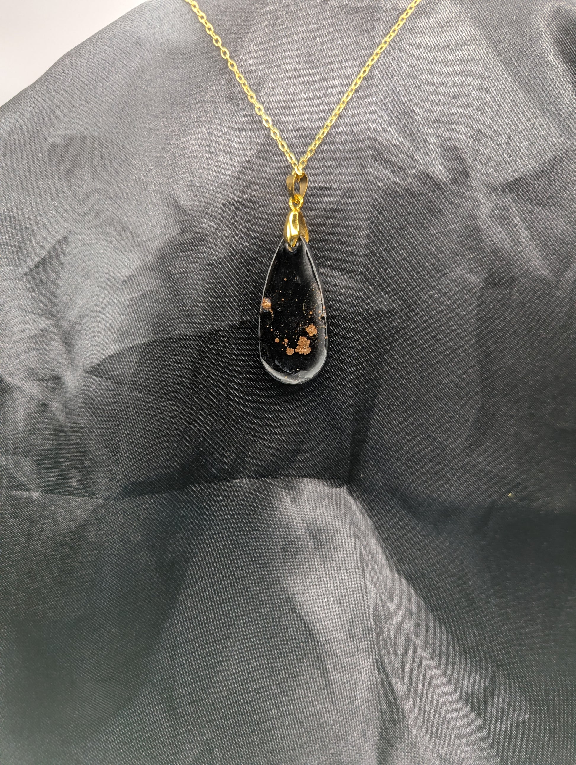 Back view of Black Resin Teardrop Pendant with specks of sparkly gold swirled inside. Pendant is on a gold pinch bail & gold plated metal chain.