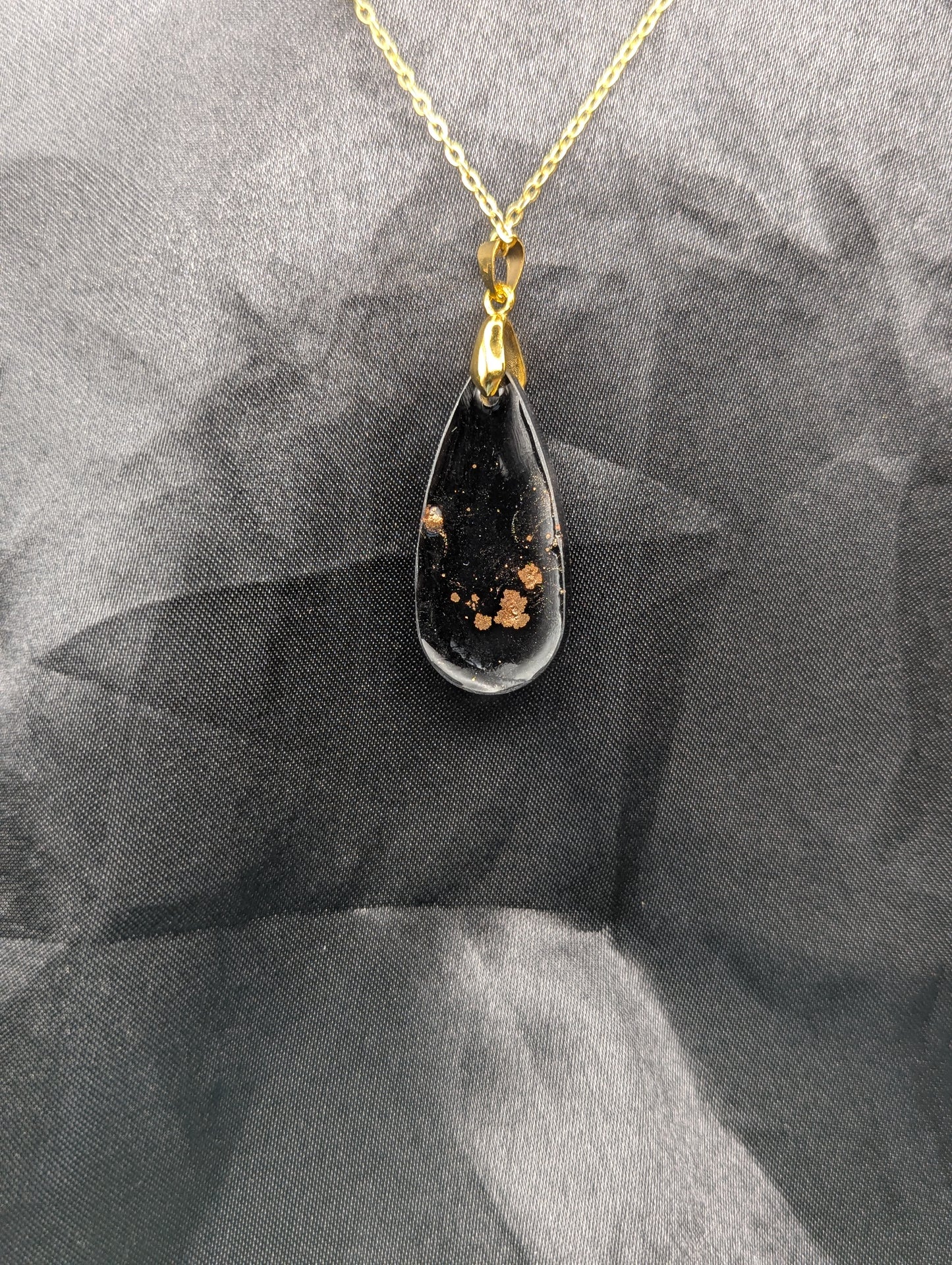 Back view of Black Resin Teardrop Pendant with specks of sparkly gold swirled inside. Pendant is on a gold pinch bail & gold plated metal chain.