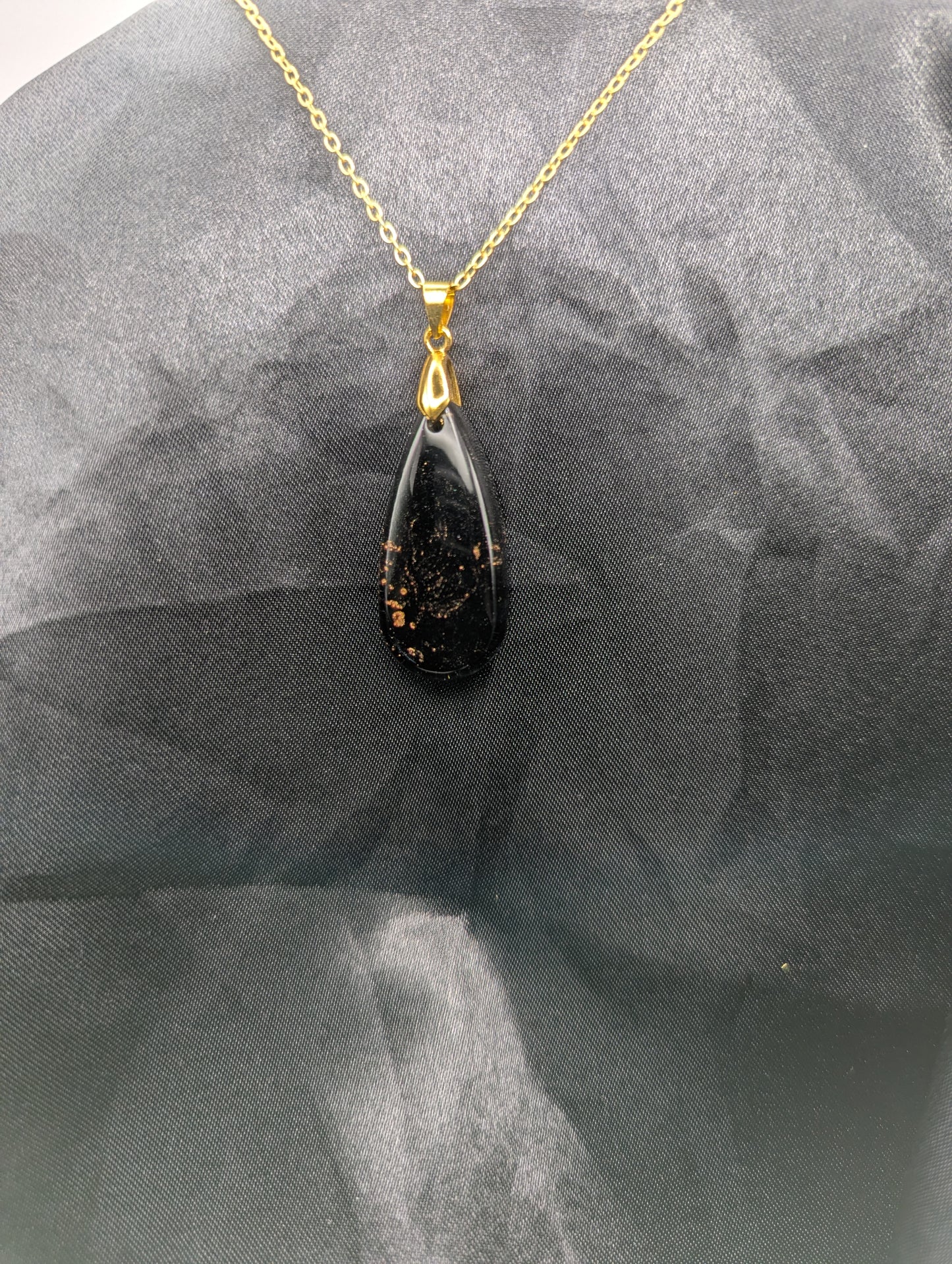 Black Resin Teardrop Pendant with specks of sparkly gold swirled inside. Pendant is on a gold pinch bail & gold plated metal chain.
