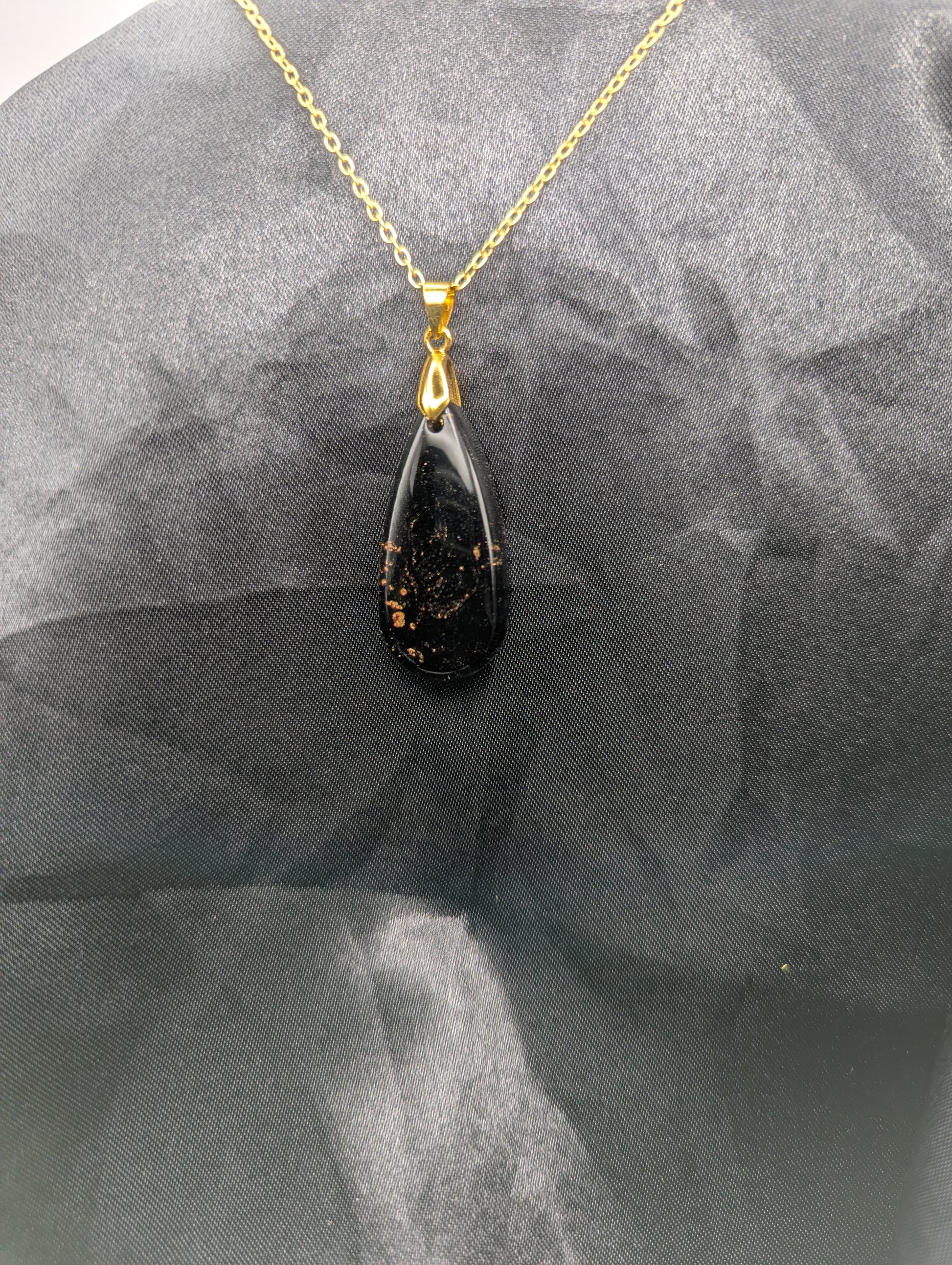 Black Resin Teardrop Pendant with specks of sparkly gold swirled inside. Pendant is on a gold pinch bail & gold plated metal chain.