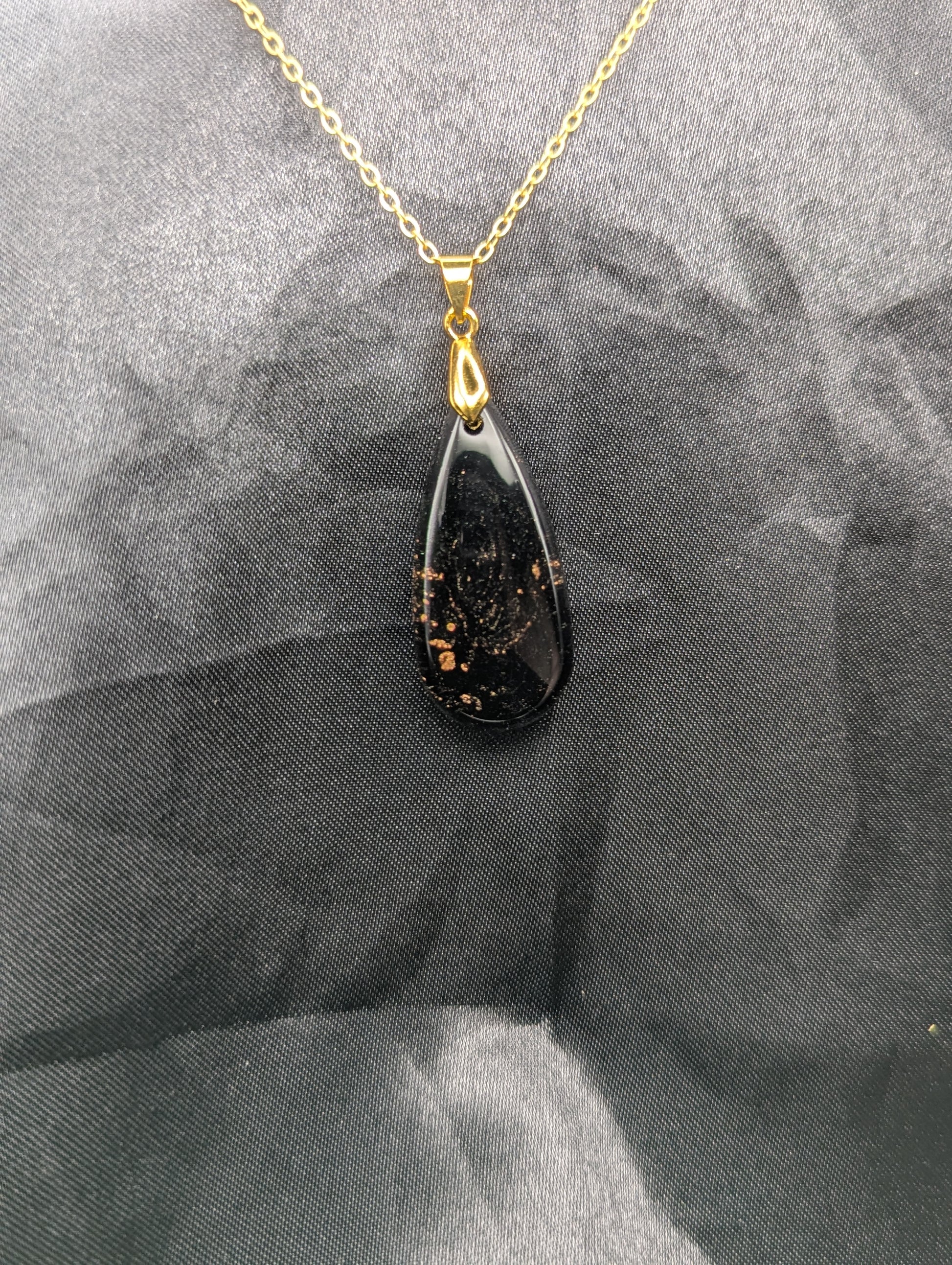 Black Resin Teardrop Pendant with specks of sparkly gold swirled inside. Pendant is on a gold pinch bail & gold plated metal chain.