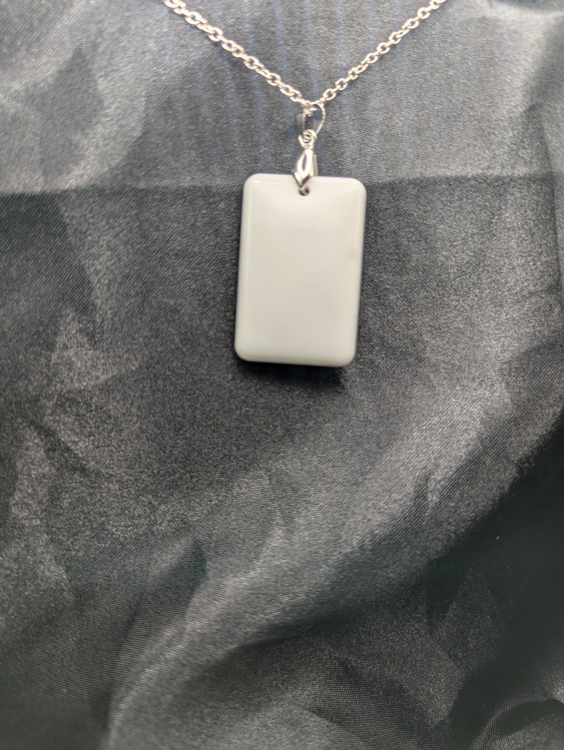Back view of Rectangle resin pendant necklace with dark red swirls and a white background. Resin necklace on a silver pinch bail & stainless steel chain.
