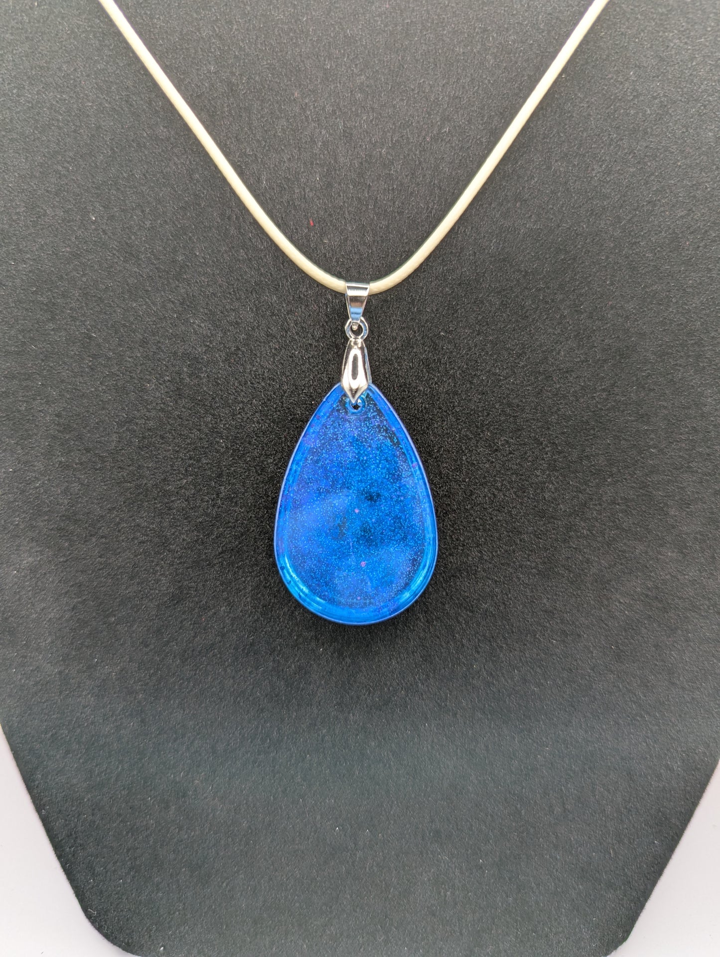 Back view of Teardrop Resin Pendant Necklace - Blue & sparkly in color with pops of bright purple. Resin necklace on a waxed cotton cord.