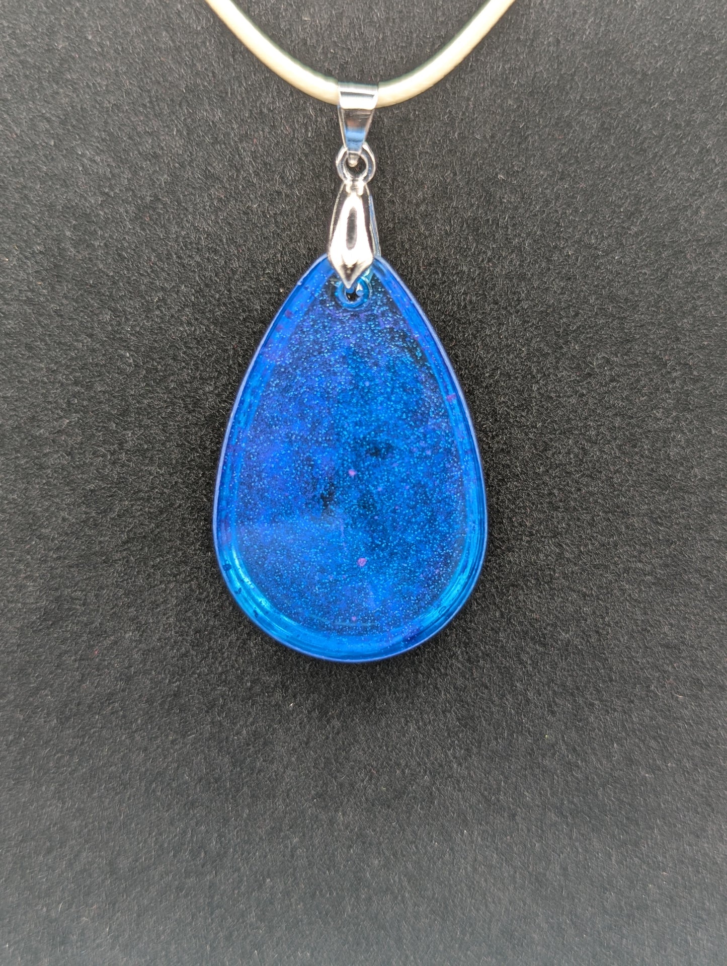 Back view of Teardrop Resin Pendant Necklace - Blue & sparkly in color with pops of bright purple. Resin necklace on a waxed cotton cord.