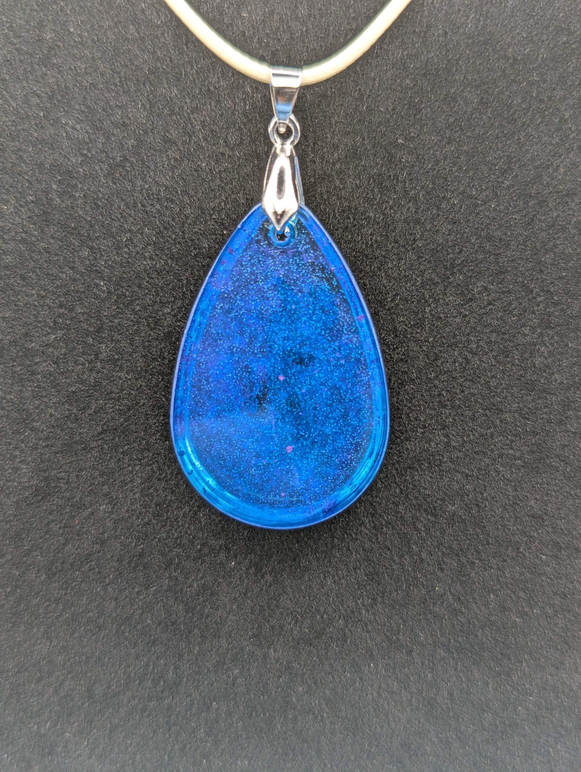 Back view of Teardrop Resin Pendant Necklace - Blue & sparkly in color with pops of bright purple. Resin necklace on a waxed cotton cord.
