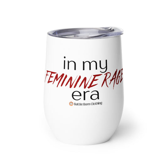 An insulated stemless wine glass with a lid for drinking wine in a tumbler. Cup is white in color with the words "in my feminine rage era". The words "feminine rage" are in red & a different font than the other words (other words are in black)
